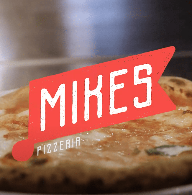 Mike's Pizzeria logo overlayed on top of photo of Mike's vegetarian wood fired pizza.